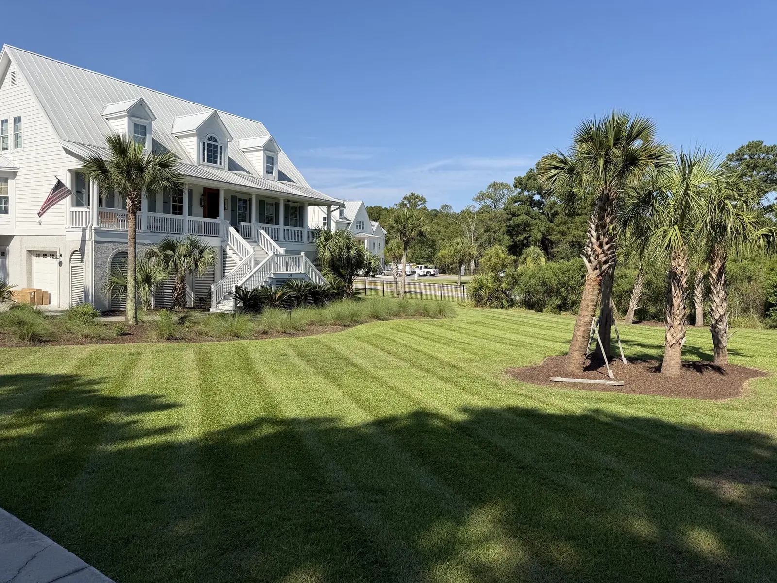 A raised coastal home on a barrier island with newly planted palms, fresh mulch beds and a striped lawn