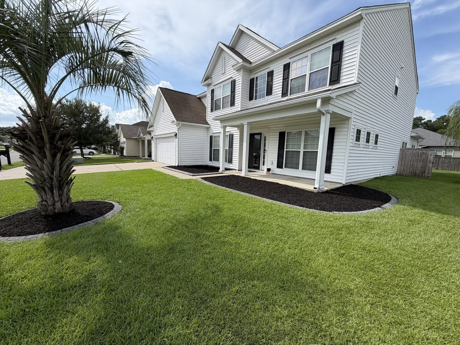 A two story Mount Pleasant home with fresh black mulch beds, a newly planted palm and a striped lawn