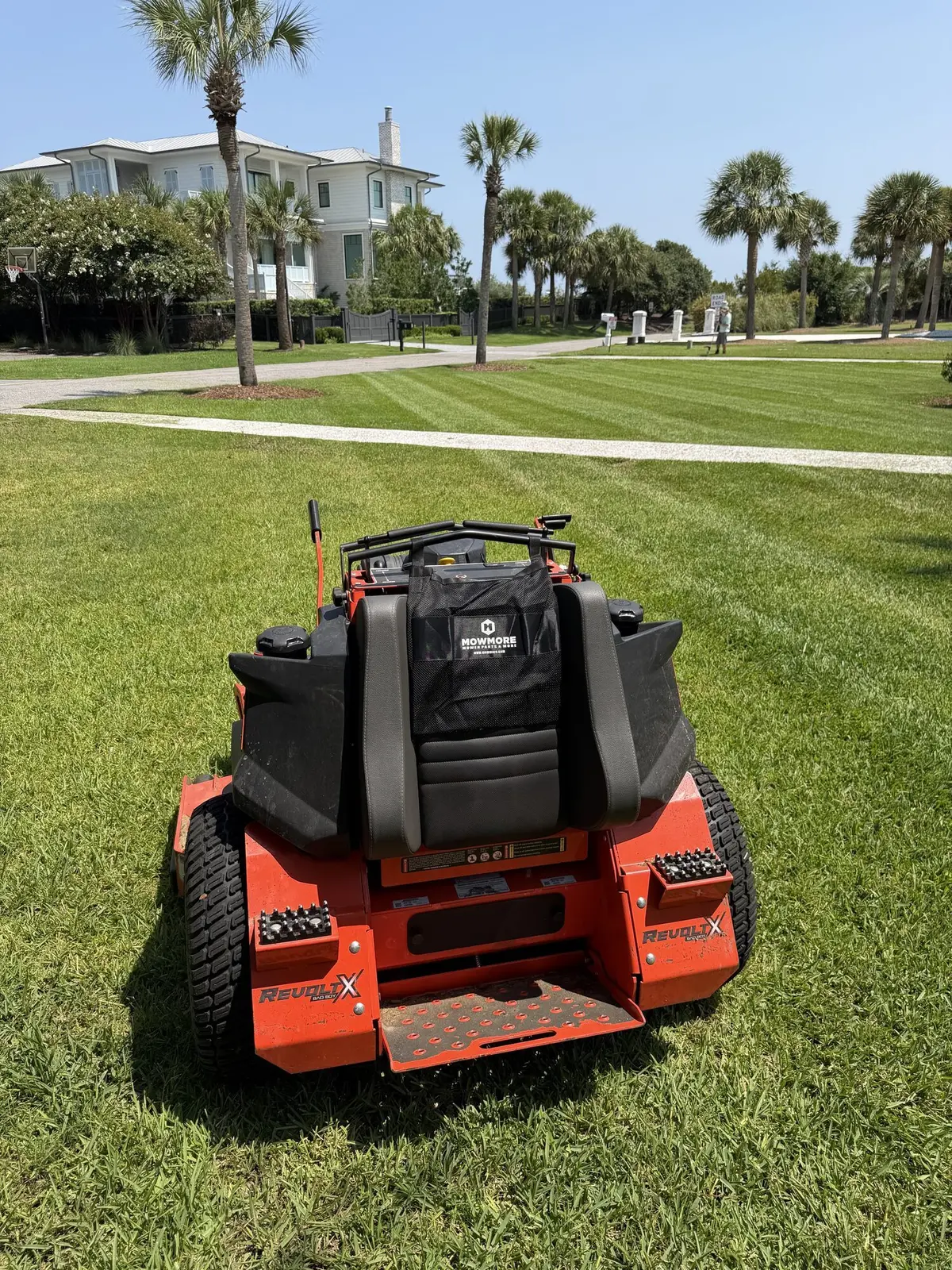 An electric zero-turn mower on a striped lawn in a palm lined coastal community