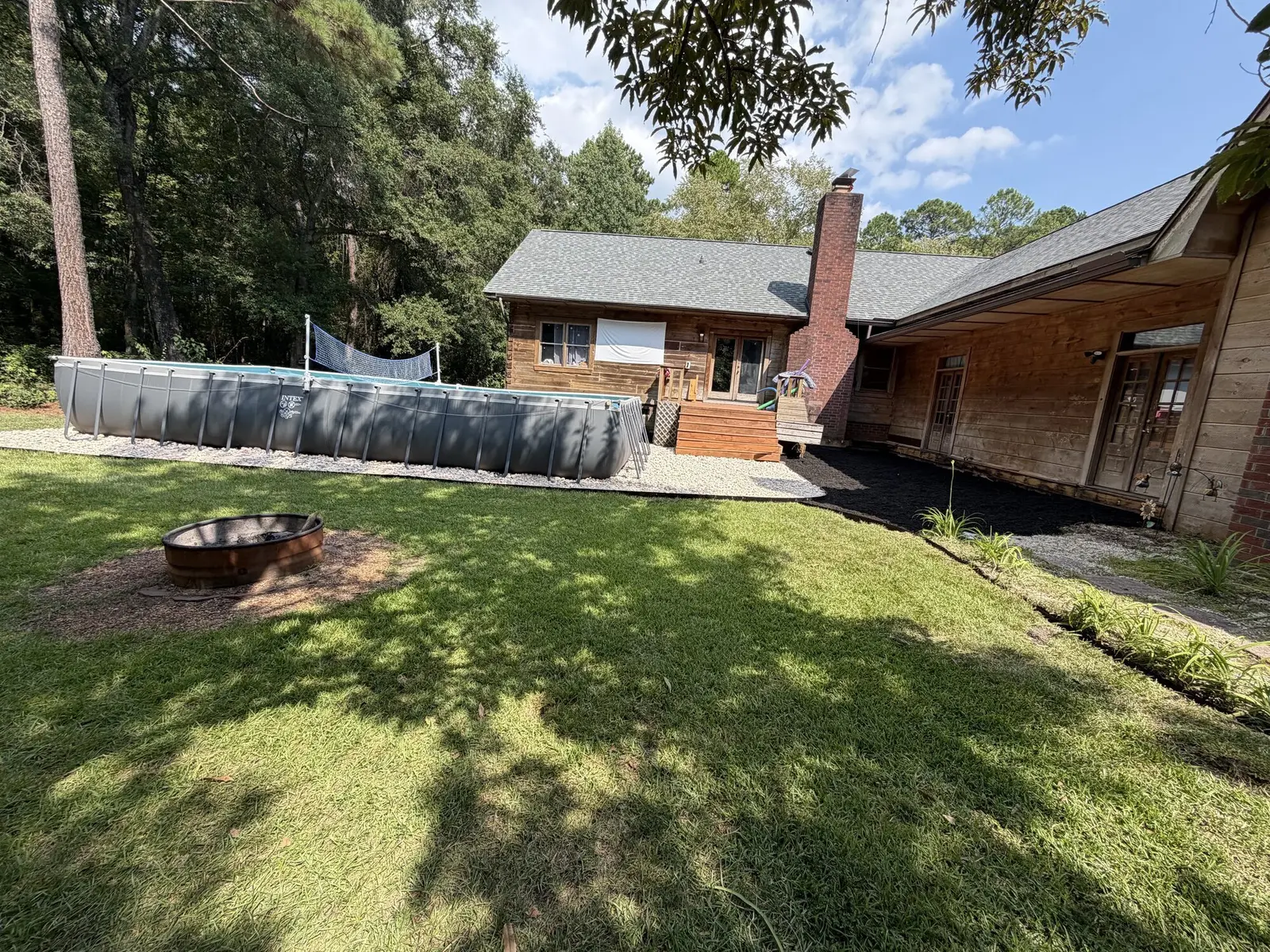 A backyard with a pool, fire pit and fresh mulch and rock bed edging