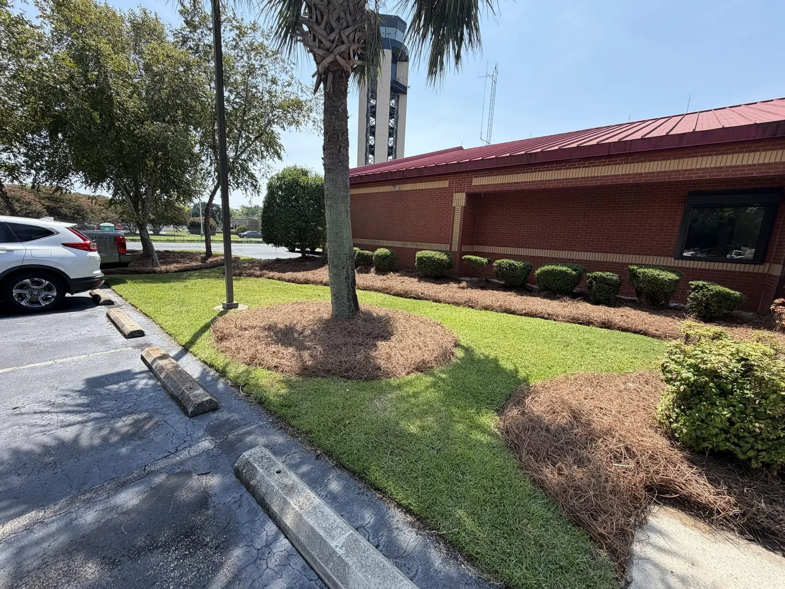 Trimmed shrubs and fresh pine straw mulch along a commercial building with a control tower