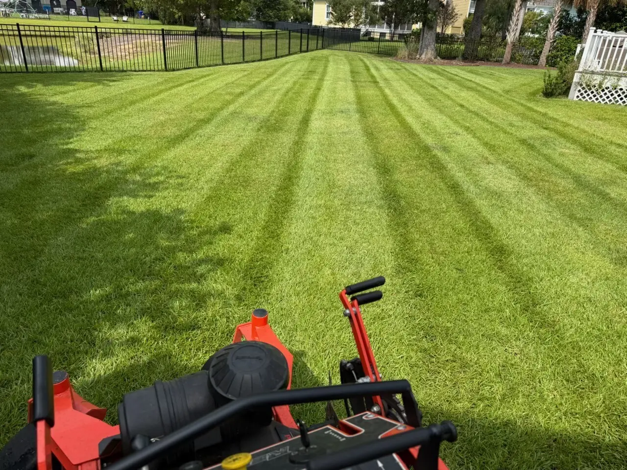 A zero-turn mower leaving crisp stripes across a backyard lawn beside a pond