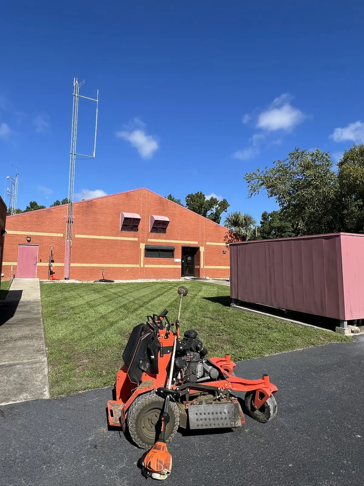 A mower and trimmer parked on a striped lawn at a commercial brick building