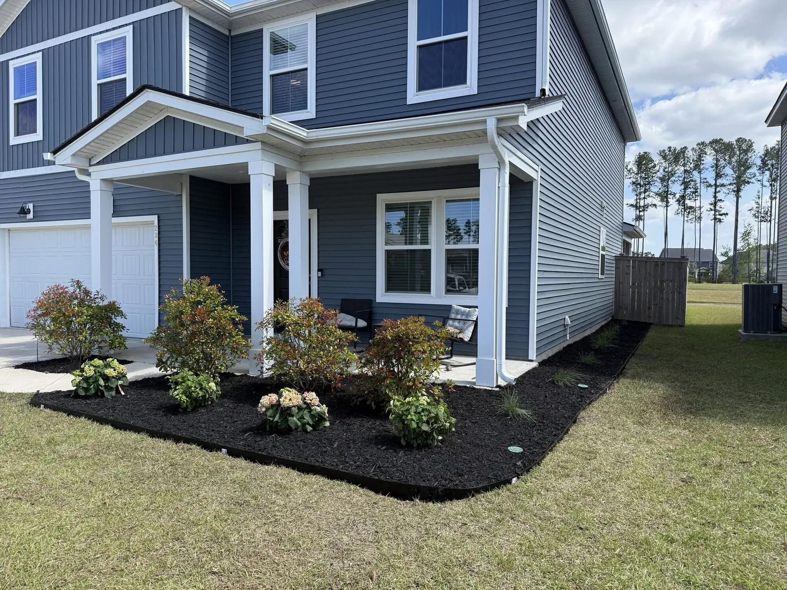 A freshly planted hydrangea bed with new mulch along a front porch